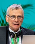 An anxious-looking older man is seen speaking from a conference dais