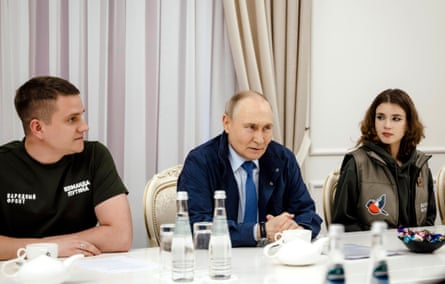 Putin sitting at a table flanked by a man and woman