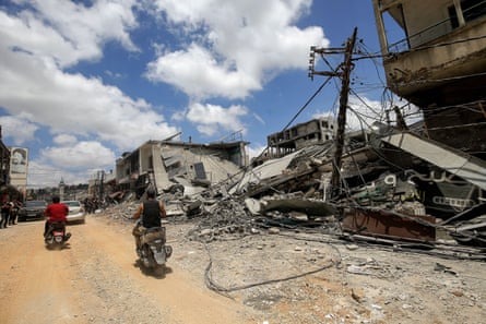 Two men ride motorcycles past destroyed buildings in Nabatieh, Lebanon.