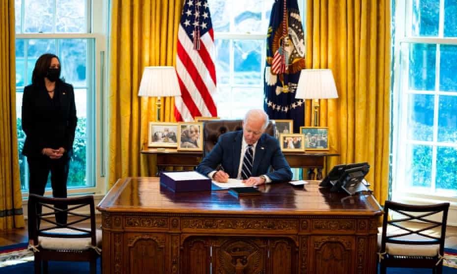 Joe Biden signs the American Rescue Plan as Kamala Harris looks on in the Oval Office on 11 March. 