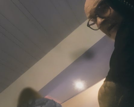 A still from undercover filming of a man’s face. He is bald and wearing glasses.