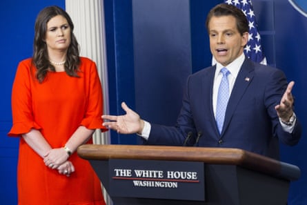 Anthony Scaramucci gesticulating while speaking at a podium with âÂÂThe White House Washingtonâ written on it, with Sarah Huckabee Sanders standing on his right with her hands clasped in front of her, wearing a bright-red half-sleeved dress