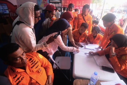 People lean in to look at a piece of paper on a table with several rescue workers in orange uniforms around them