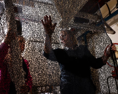 Two women standing behind a sheet of lace, one of them inspecting it closely