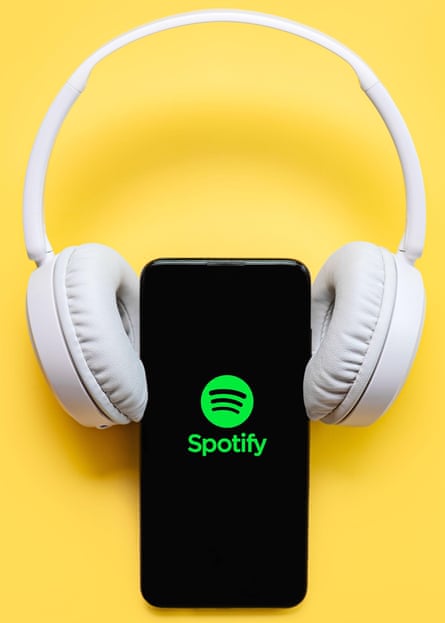 Spotify application icon on black screen of smartphone with white wireless headphone on yellow background