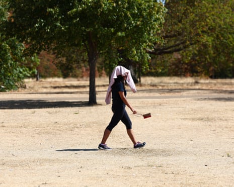 A walker drapes a jacket over her head to shield her face from the sun in a park
