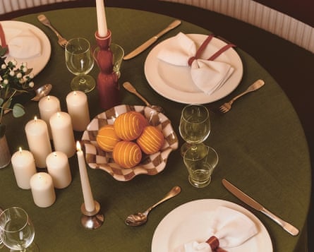 A table set with white candles and a green tablecloth with red napkin ribbons on white napkins shaped like bows