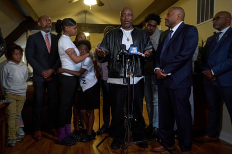 A man speaks at microphones, surrounded by family and a legal team