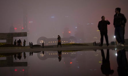 People walk on the Bund in front of the financial district of Pudong during a hazy night in downtown Shanghai