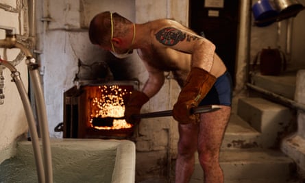 A tattoed man in shorts pokes a stove in Rajaportti sauna