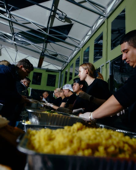 People wearing black clothes and white gloves stand over trays of food.