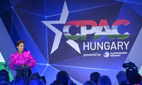Woman in pink speaking on stage with CPAC Hungary behind her
