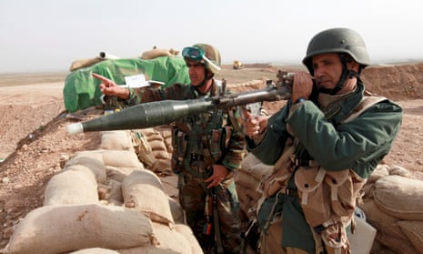 Kurdish peshmerga soldiers aim guns across a wall of sandbags