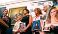 a man speaks while women hold photos of children