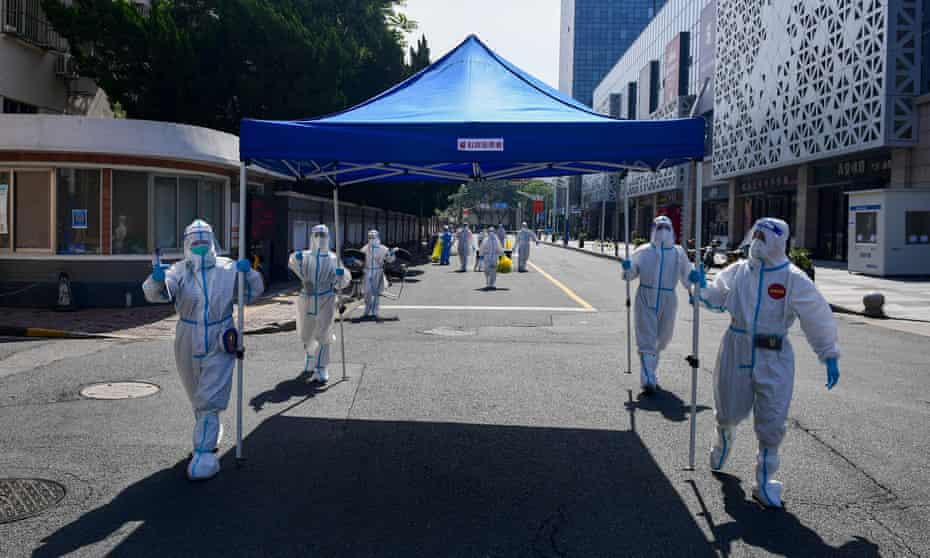 Workers in protective suits move equipment for a makeshift nucleic acid testing site in Shanghai, China