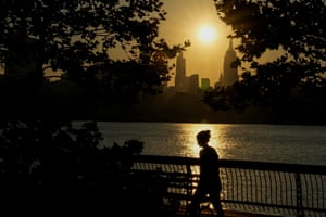 The sun rises over New York City skyline as a person walking is silhouetted along the riverfront