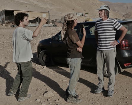 Three people standing near a car in a desert area