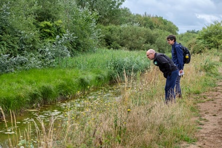 Two men look at a stream or pond.