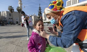A Palestinian volunteer paints a child’s face at Manger Square, in the Church of the Nativity, ahead of scaled-back celebrations for Eastern Orthodox Christmas due to the coronavirus pandemic, in the West Bank city of Bethlehem, Tuesday, 5 January, 2021.