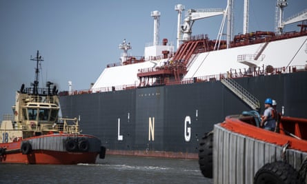 A navy and white painted tanker with two tugboats, one on either end of the ship, in water.