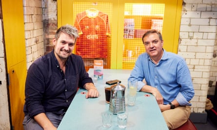 Two men, both wearing blue shirts, sitting at a restaurant table talking