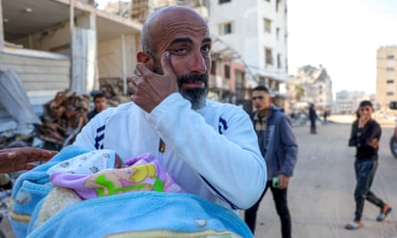 A man holding a baby wipes away a tear outside al-Shifa hospital in Gaza City