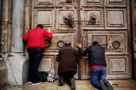 Worshippers kneel and pray in front of the closed doors of the church