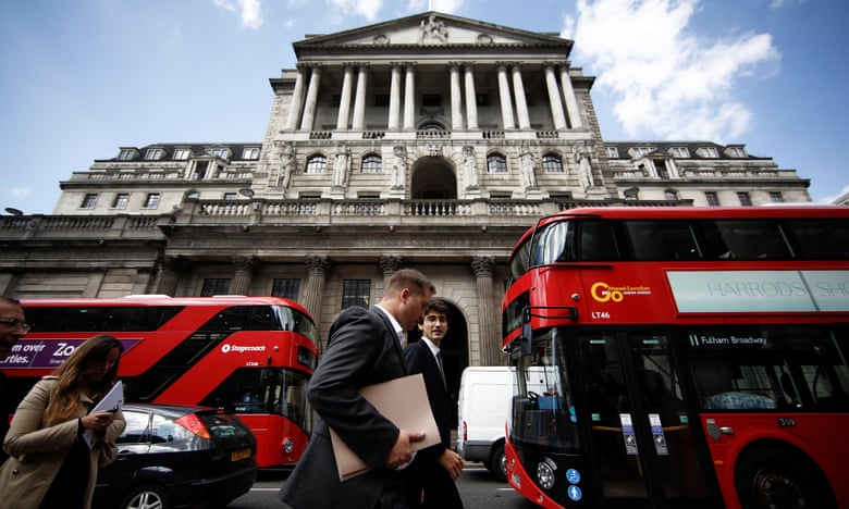 Businessmen pass red London buses outside the Bank of England in the City of London.