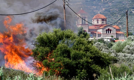 Bushes and trees burn with a church and telephone poles in the background