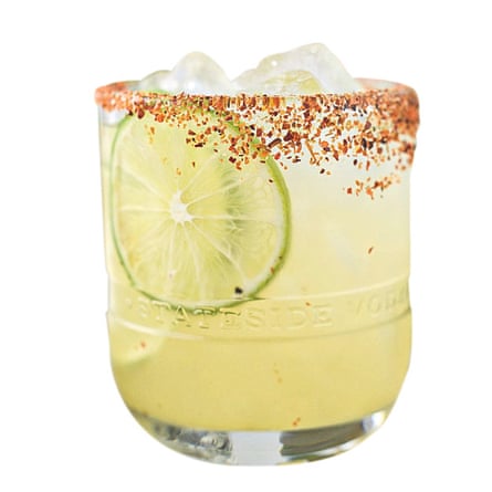 A tumbler containing a lime-coloured cocktail with a slice of lime and ice cubes, with a chilli powder and salt rim
