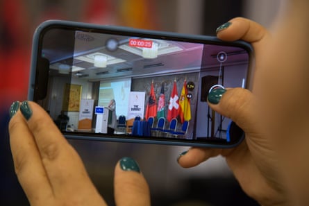 A woman’s hands holding a camera that is recording one of the speakers at the conference.
