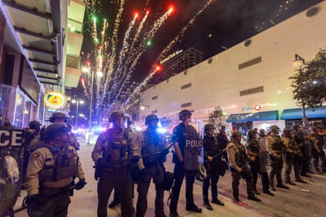 Fireworks explode behind Police officers in riot gear during a demonstration following federal immigration operations in Los Angeles on June 9, 2025.