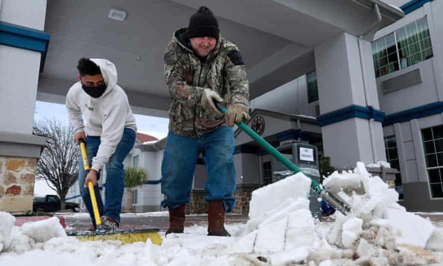 Sam Patel (L) and Mike Bollin (R) clear snow from the front of the SureStay Plus Hotel which is completely full with guests that have no power at home, in Benbrook, Texas, 16 February 2021.