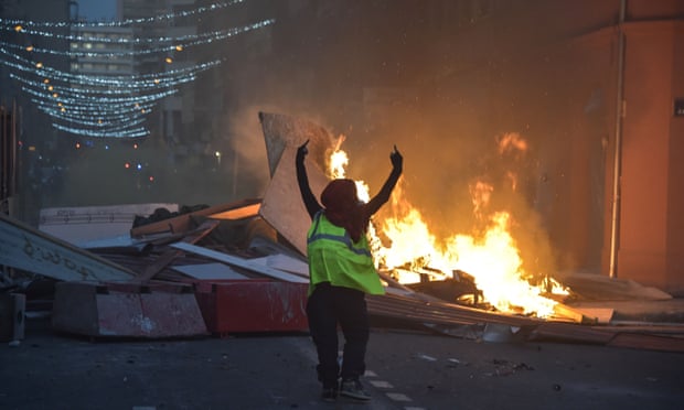 A gilet jaune demonstrator gestures in front of a burning barricade in Toulouse.