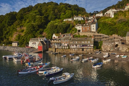 Boats moored in the sea in a stone harbour with old houses and cottages climbing the hillside beside them.