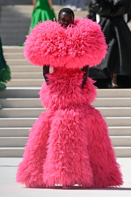 A model walks down a catwalk at Balenciaga wearing a striking bright pink couture gown covered in dense, fluffy, feather-like texture from shoulders to hem.