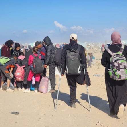 Crowds of people carry bags along a dusty path.