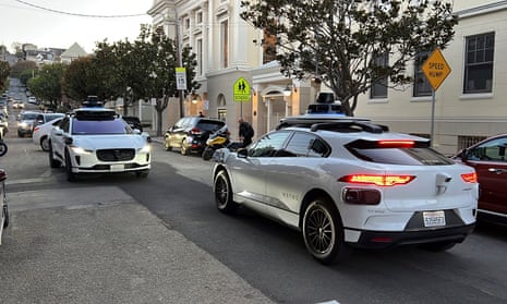 Two driverless Waymo taxis face off on a street in San Francisco before driving past each other.