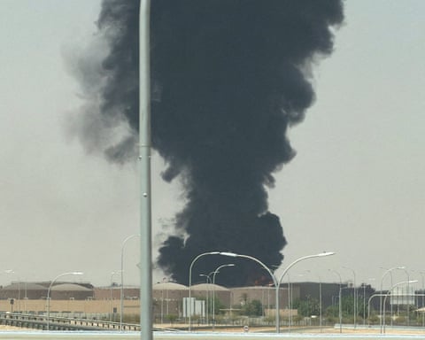 A large plume of thick black rising above fuel storage tanks
