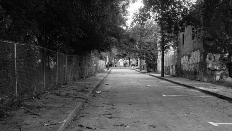 a empty street; one side is lined with trees behind a metal fence