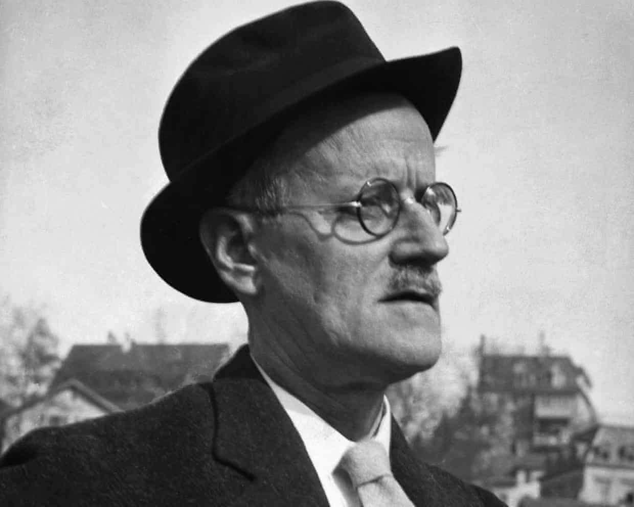 Black and white photo of man in round spectacles and hat, wearing a suit and tie.
