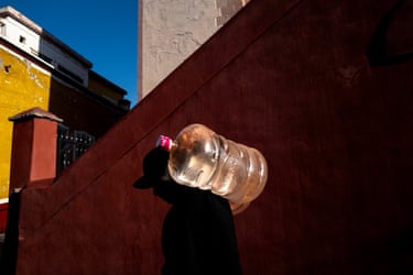 A large water bottle projects from a wall at 90 degrees. No clue is given to how it suspends there, but the shadow of a man walking past makes it look like the bottle is resting on his shoulder
