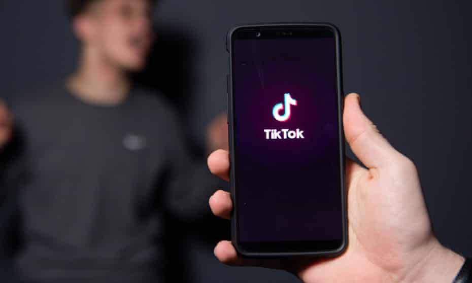 Phone with TikTok icon in hand and man in the background