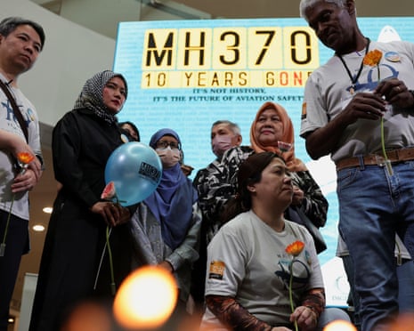 People gather around candles, with a display board behind with the words 'MH370 - 10 years gone' on it