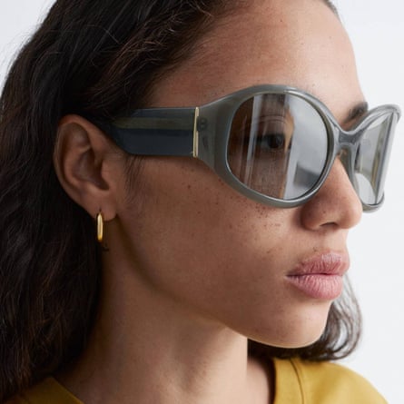 A model wears oversized oval sunglasses. The shaded lenses are light enough to see the eyes through