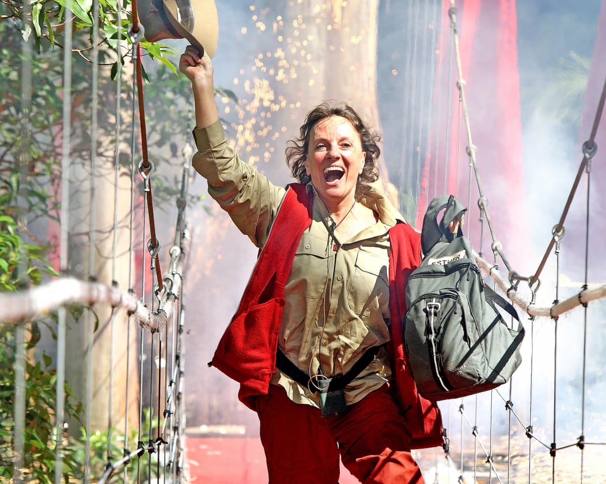 Esther Rantzen running across a drawbridge waving a hat and carrying a bag