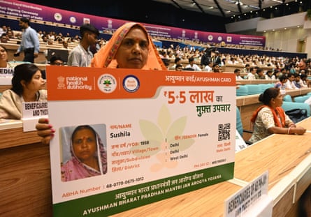 An older Indian woman in a conference hall holds an oversized mock-up of her health ID card