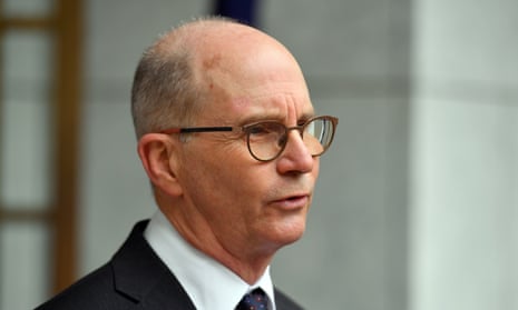 A headshot of Paul Kelly talking to the media wearing a suit and glasses