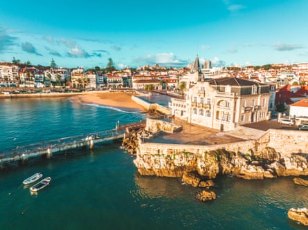 A seaside town with a rocky and sandy shore and white buildings with red tiled roofs