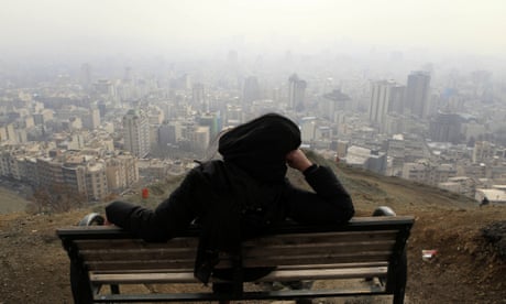 Woman in burqa looking out over polluted skyline of Tehran